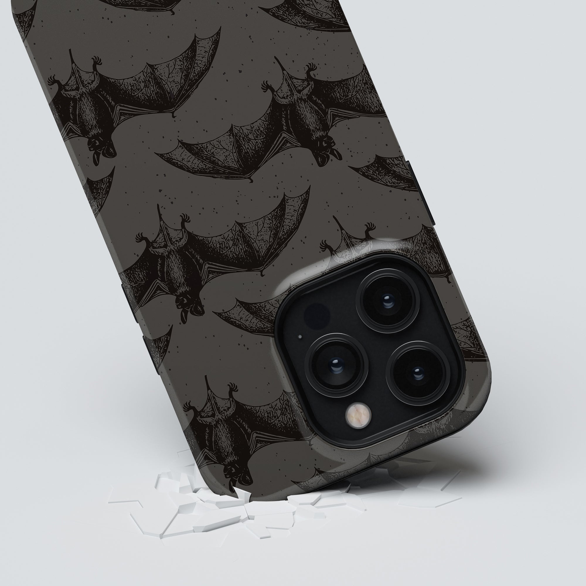 A smartphone encased in the Bats - Tough case rests on a white surface with a few small broken pieces around it.