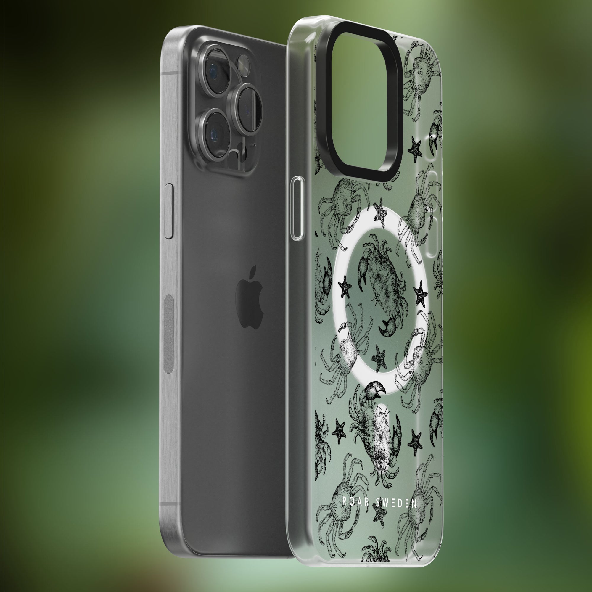 A silver iPhone with a detachable, transparent phone case featuring an ocean-themed accessory design of crabs, stars, and the phrase "Black Crab - MagSafe," shown against a blurred green background.