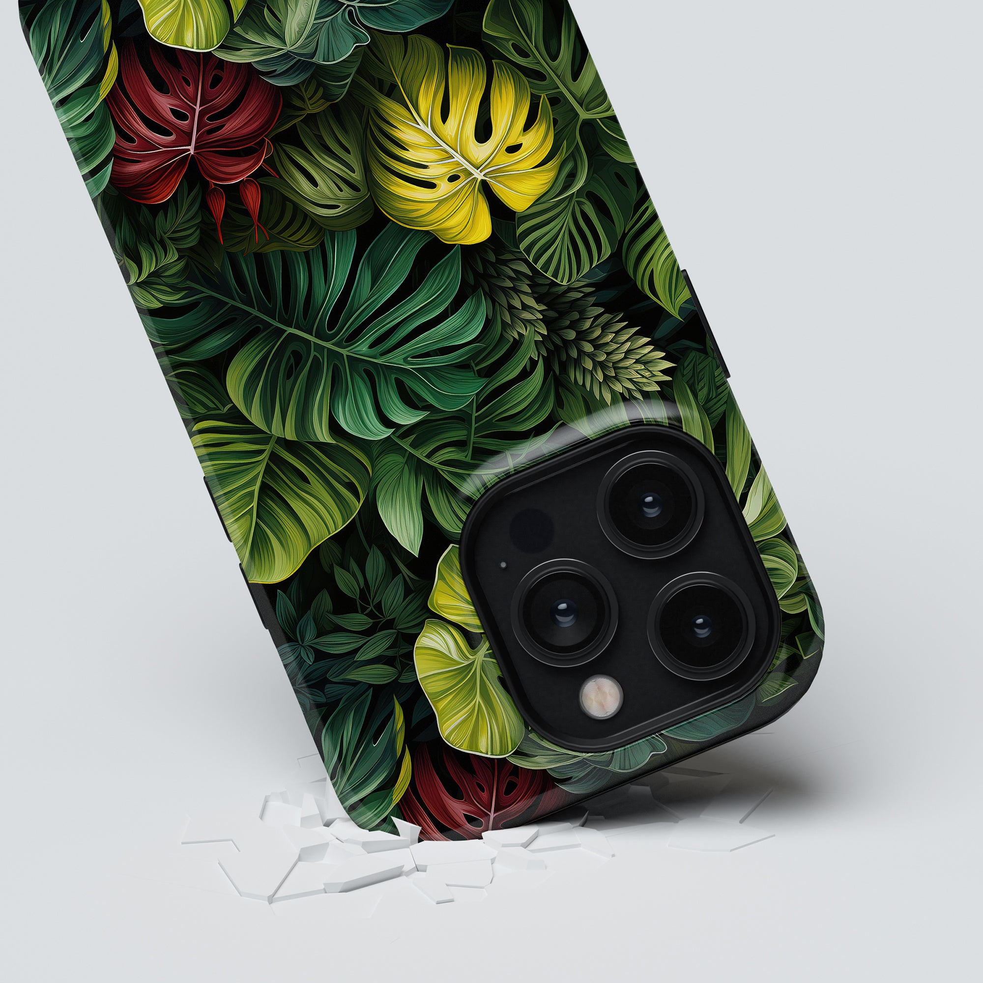 A smartphone with a Deliciosa - Tough Case from the Jungle Collection lies face down on a white surface, surrounded by pieces of a broken screen protector.