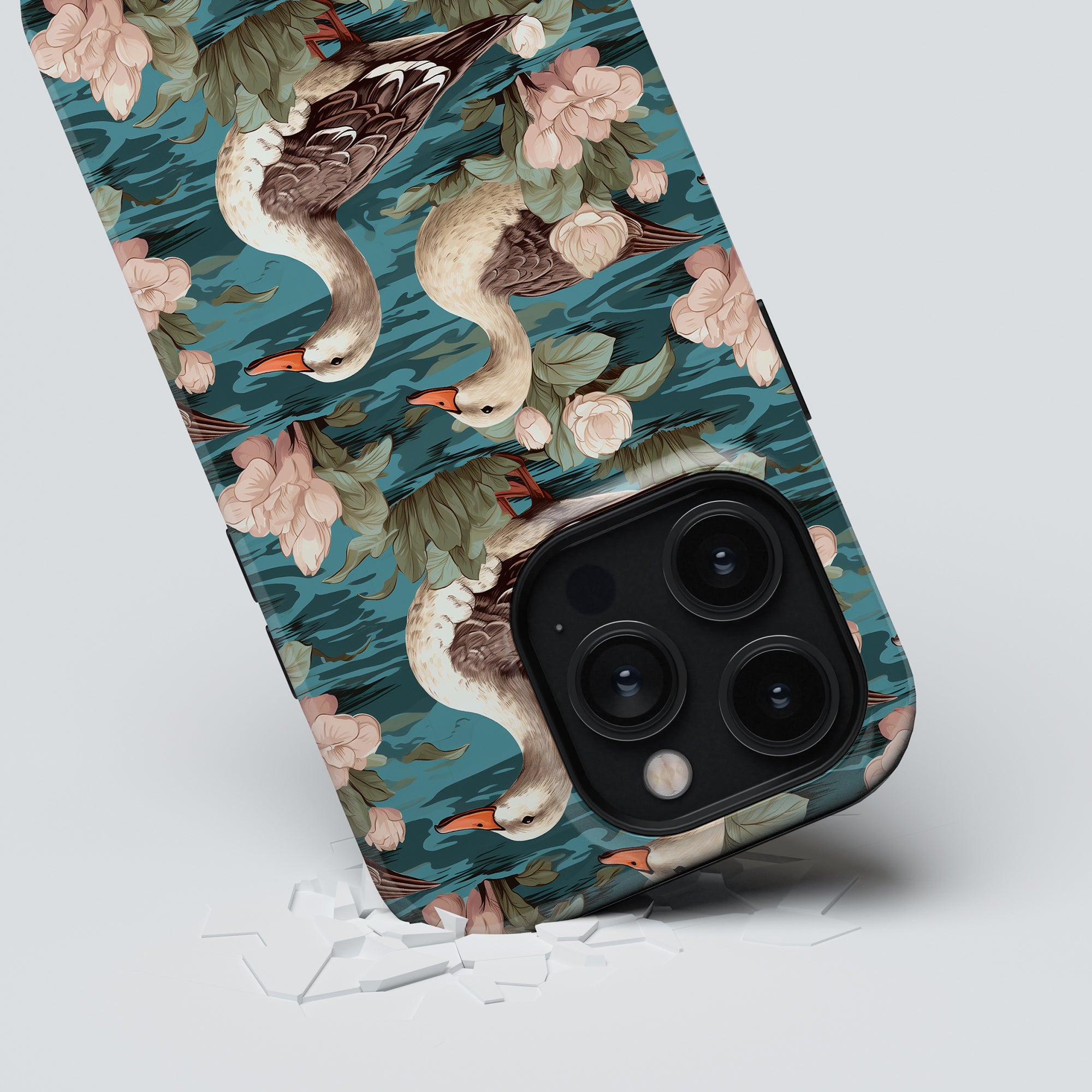 The Duck Pond - Tough case, featuring a charming floral and duck pattern, leans on a gray surface next to broken glass pieces, showcasing its blend of beauty and durability.