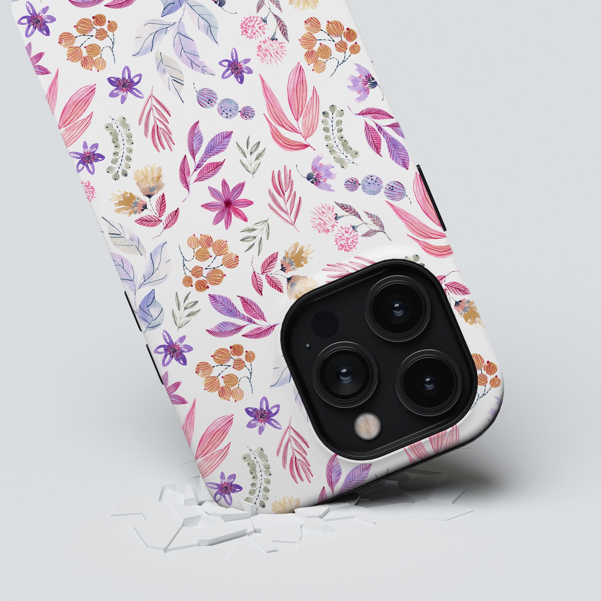 A smartphone from the Floral Collection with a Flower Power - Tough Case rests on a light surface with cracks beneath it, suggesting it has been dropped. The phone's camera lenses are prominently visible, showcasing the maximalt skydd it offers.