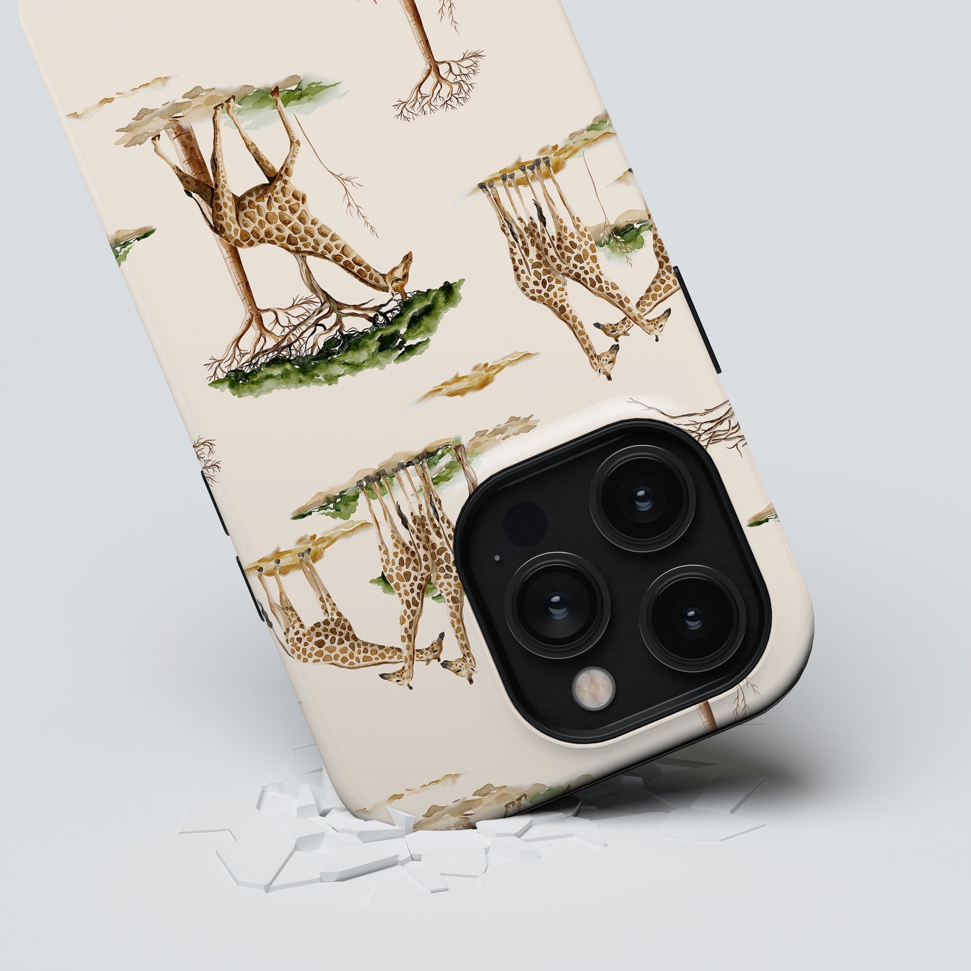A smartphone with a Giraffa - Tough Case rests on a white surface, with several pieces of polymer from the case scattered around. The phone's triple camera lenses are prominently visible.