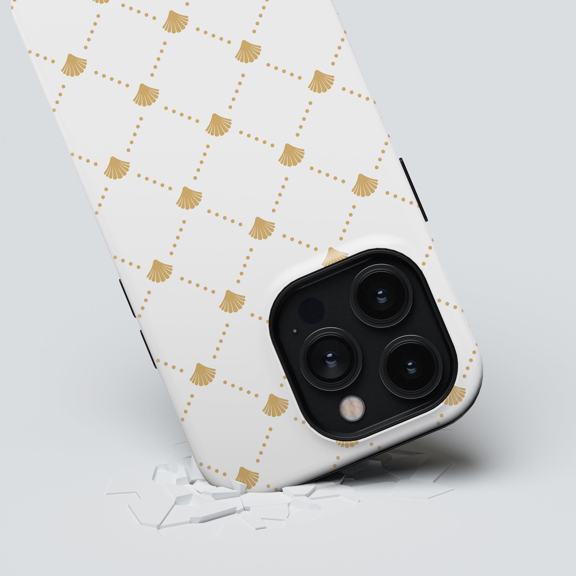 A Luxe Shells White - Tough Case, marked by its elegant gold pattern, lies face down on a cracked surface. Featuring a triple camera setup, this tough case from the Ocean Collection ensures both protection and style.