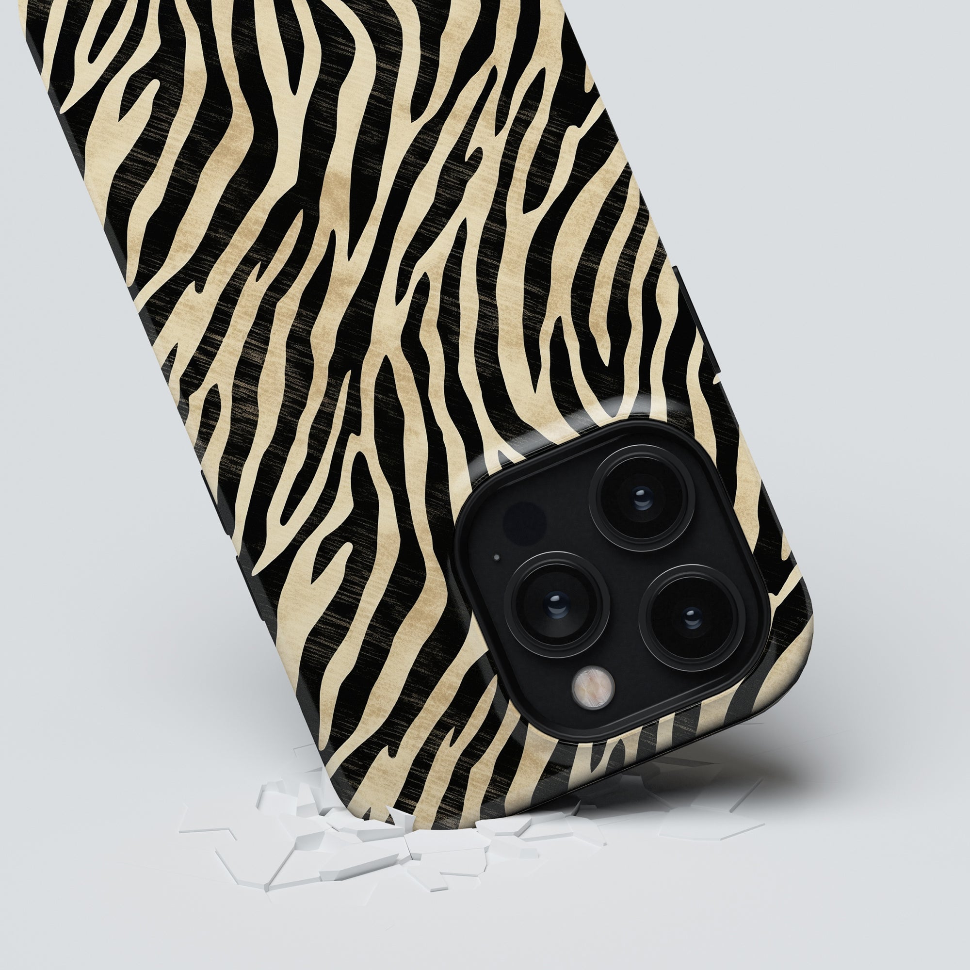 A smartphone with a zebra print case from the Zebra Collection lies on a surface, surrounded by shards of broken glass, showcasing the Marty - Tough Case's robust skydd.