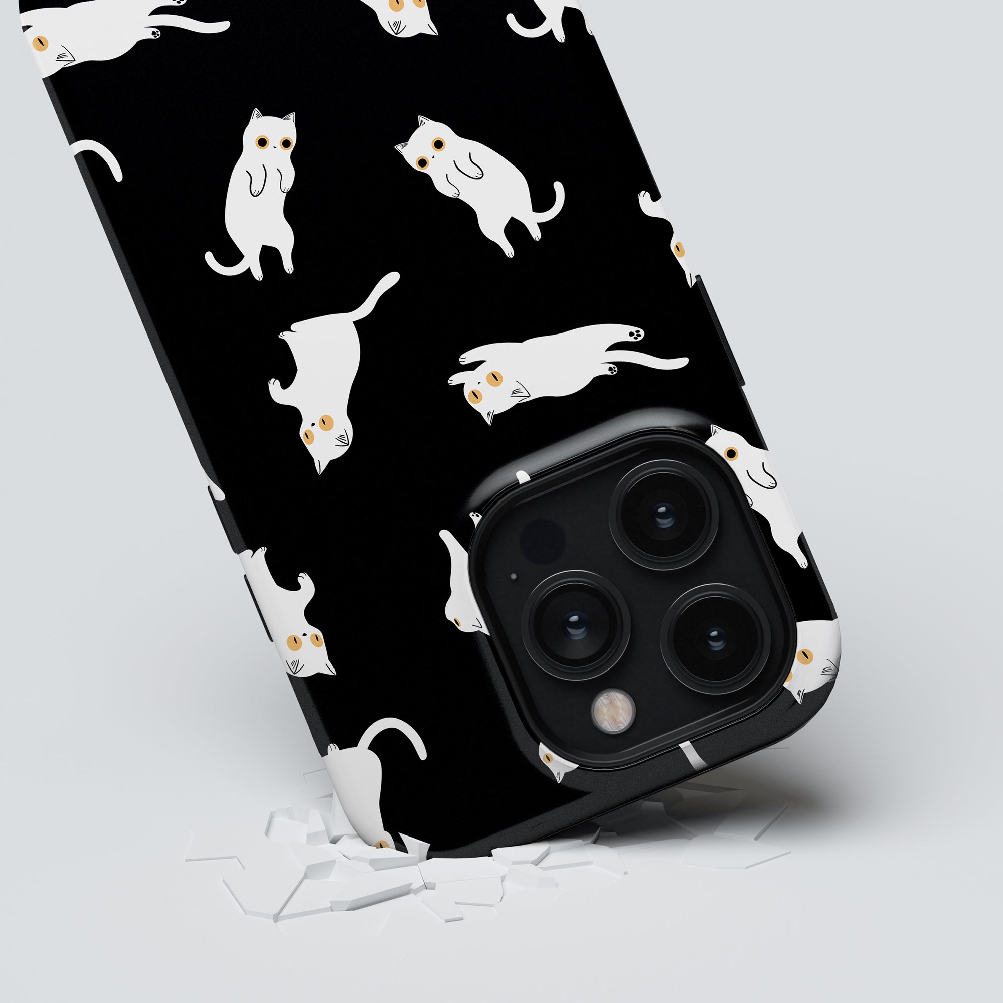 A Night Cat - Tough Case smartphone features a black background with white cats and vivid orange eyes, resting on a surface sprinkled with tiny white fragments.