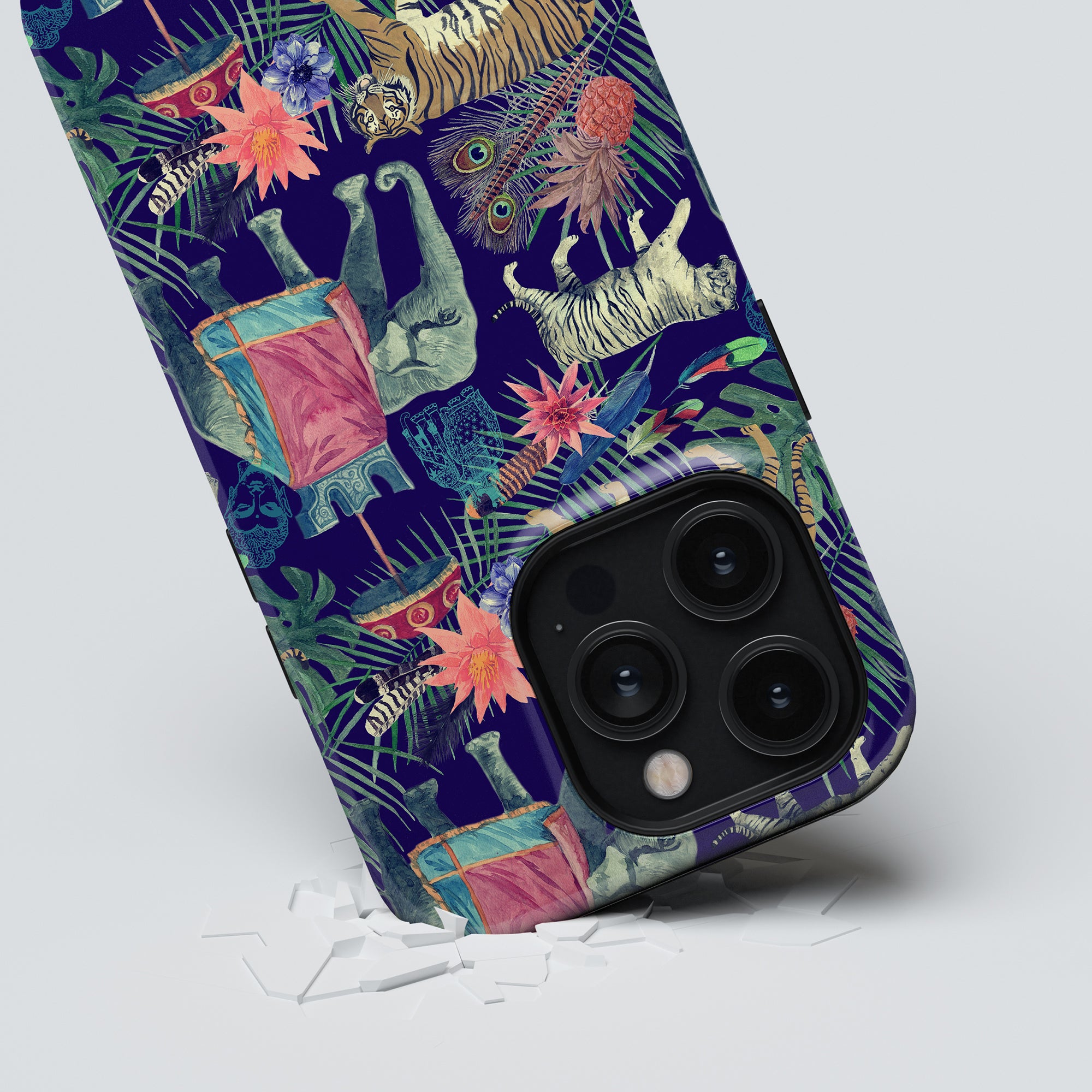 A smartphone with a colorful jungle Bombay - Tough Case resting on a white surface with a broken piece near the camera lenses.