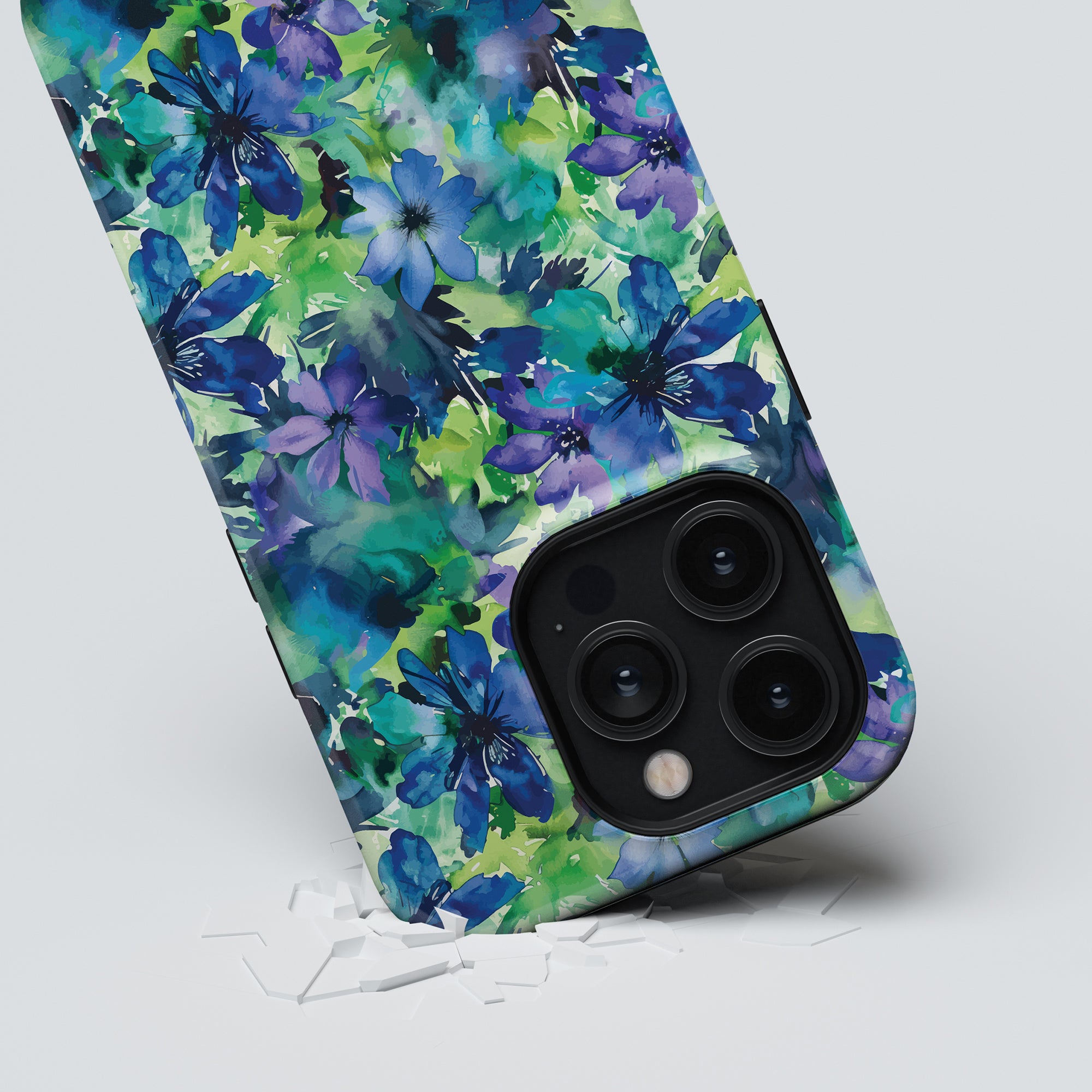 A smartphone from the Floral Collection, adorned with a green and blue floral patterned Sweet Flower - Tough Case, rests against a light background with scattered white pieces around it. The camera lenses are visible.