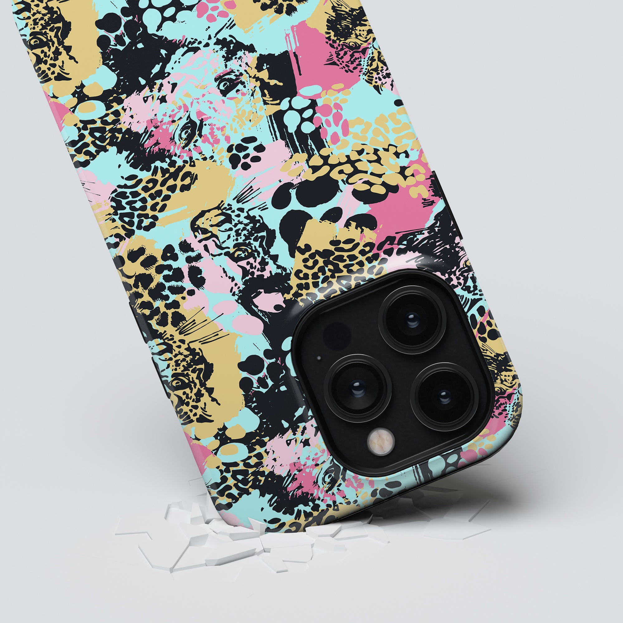 A smartphone with a leopard print and abstract colorful design on its Bite tough case, featuring a prominent triple-lens camera, partially peeling from a grey surface.