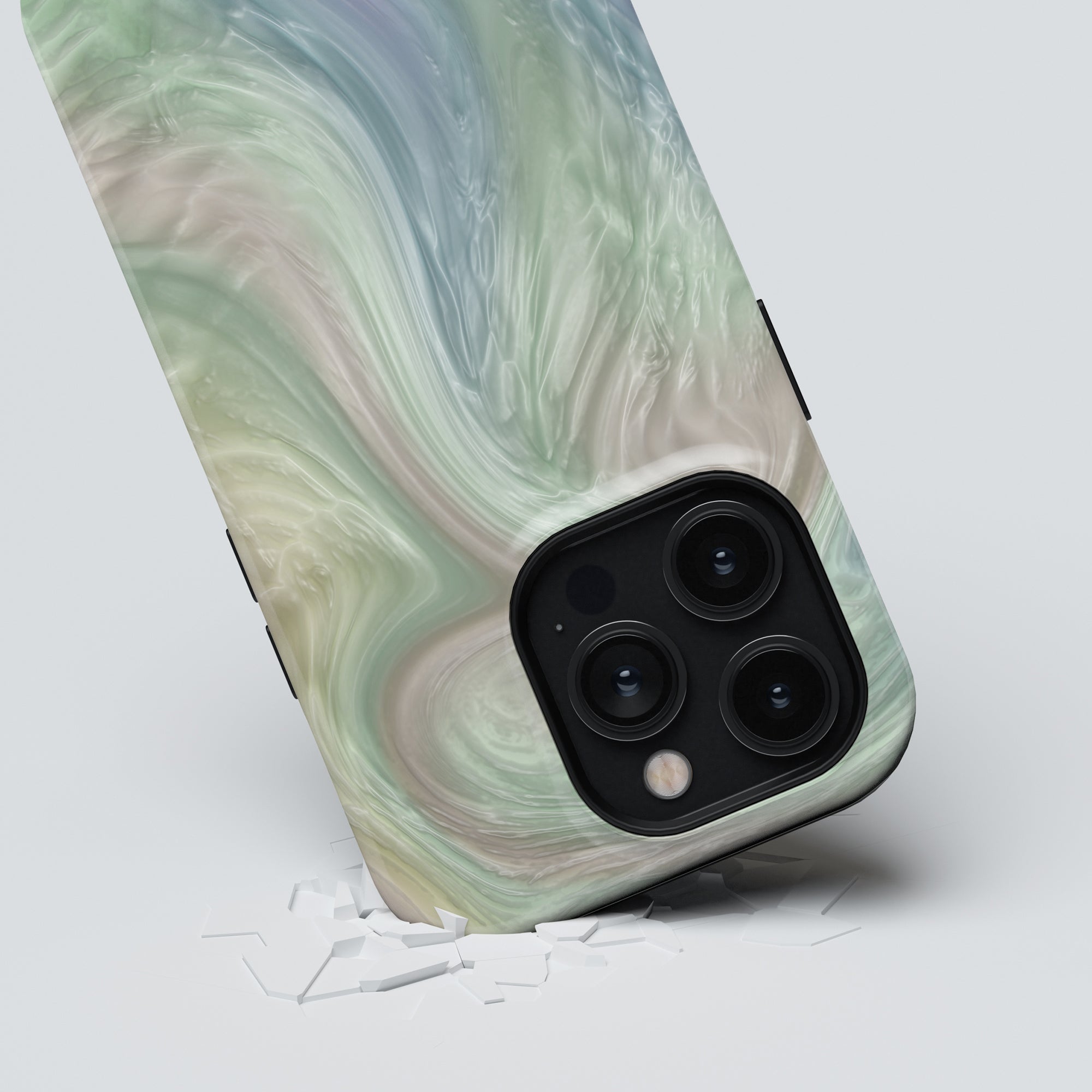 A smartphone with a marbled green Nacre - Tough Case lying on a white surface, with its triple-lens camera facing up and glass fragments scattered nearby.