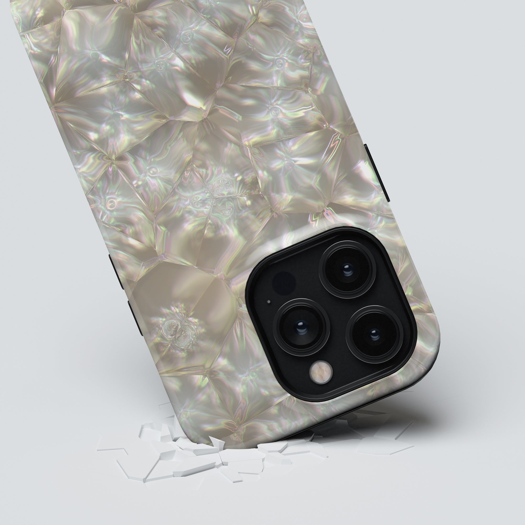 A smartphone with a reflective, textured Pearls - Tough Case and a triple-lens camera, lying on a surface with glass shards scattered near it.