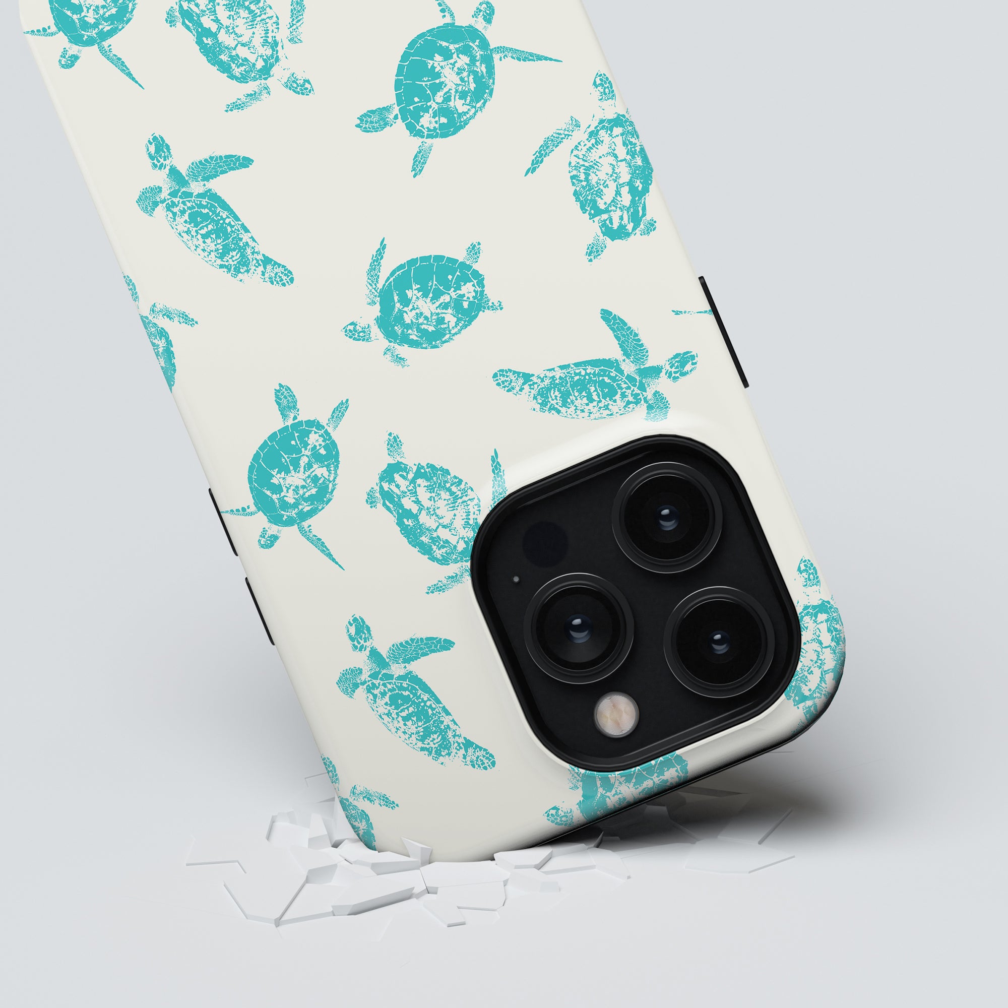 A smartphone with a Sea Turtles - Tough Case from the ocean collection partially obscuring the camera lenses, resting on a cracked surface, designed for phone protection.