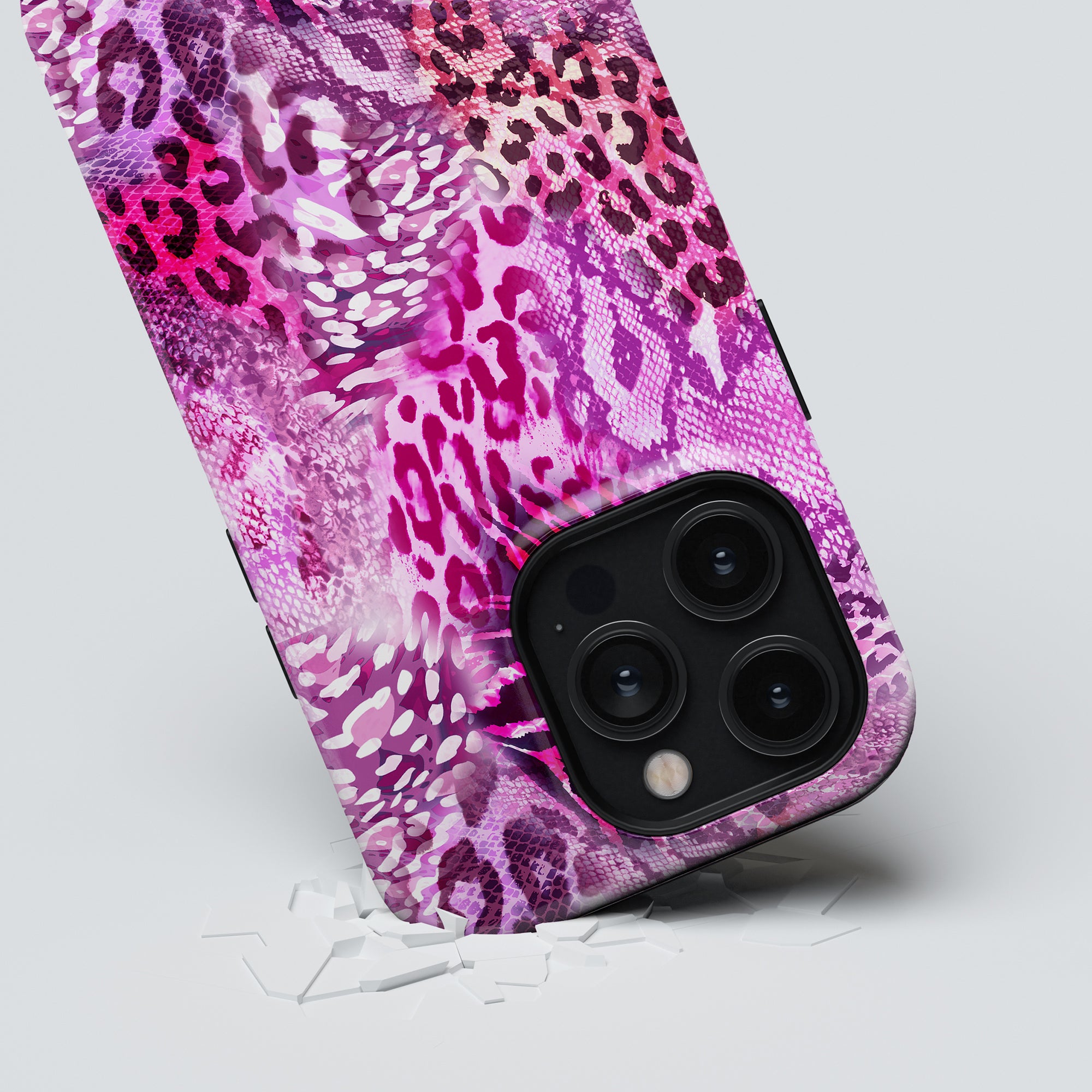 A smartphone with a Swirl Leopard tough case from the Hybrid Collection, featuring a triple-lens camera, partially submerged in a shattered glass surface.