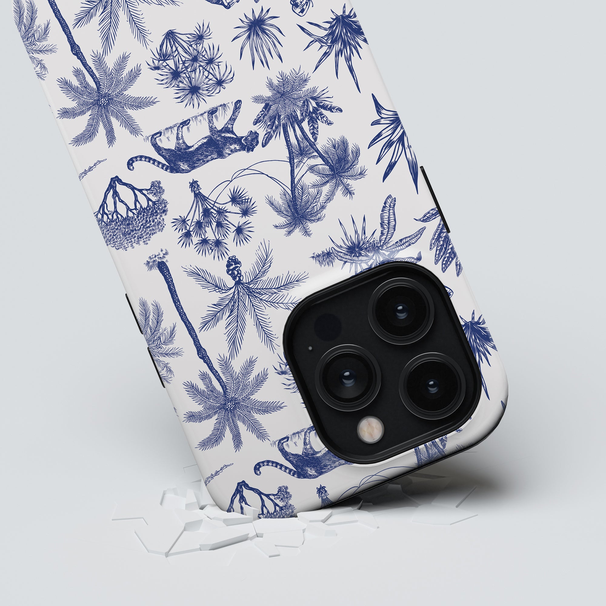 Tough Case with a triple-lens camera breaking through a sheet of paper with a blue Toile De Jouy botanical print.