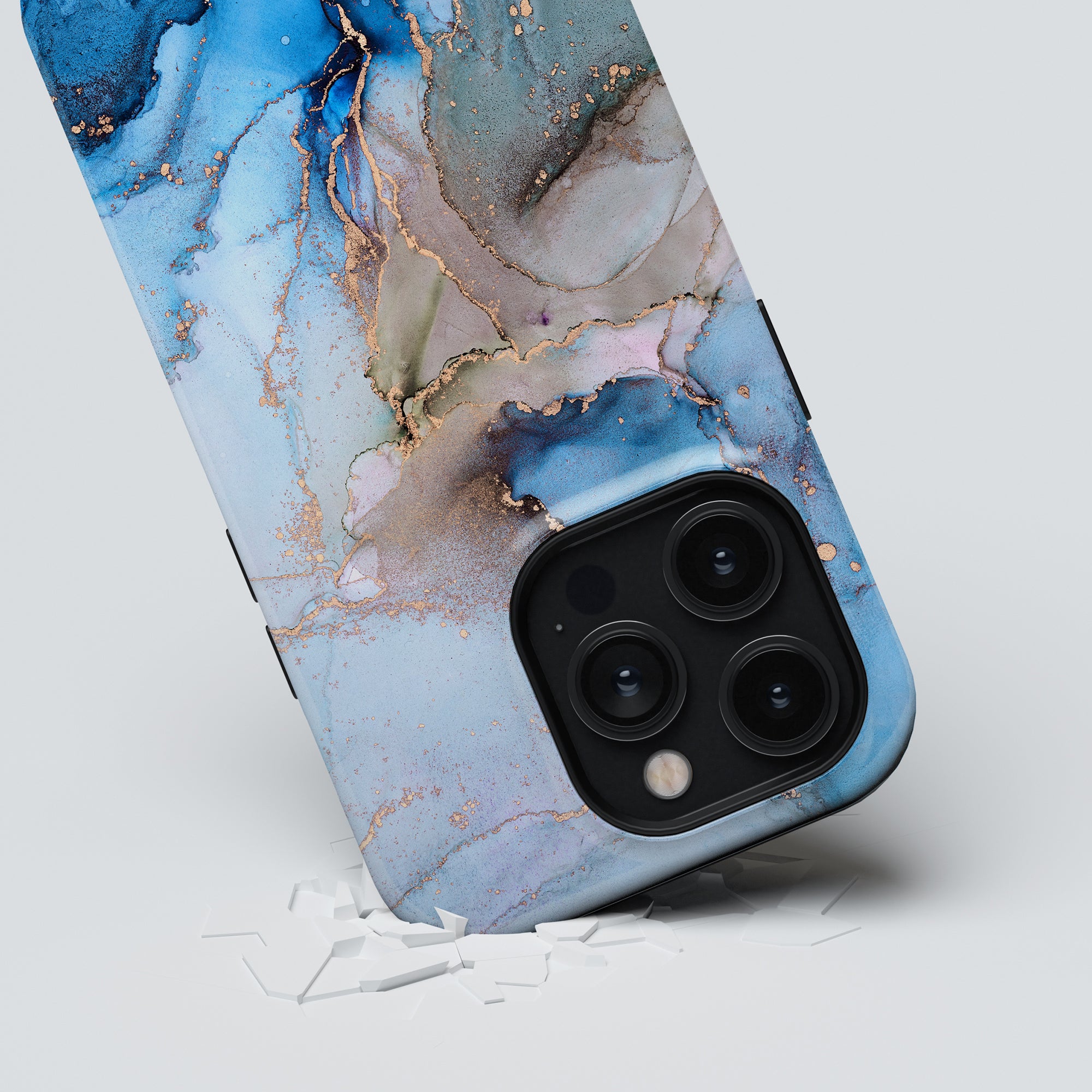 A Waves - Tough Case featuring a marble design in blue and gold rests on a white surface, surrounded by shattered glass pieces.